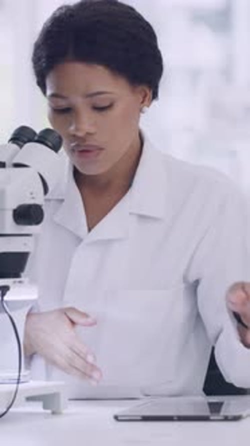 Young Woman Using Microscope and Tablet in Laboratory
