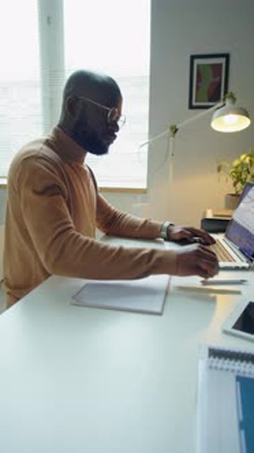 Black Businessman Using Laptop and Taking Notes in Office