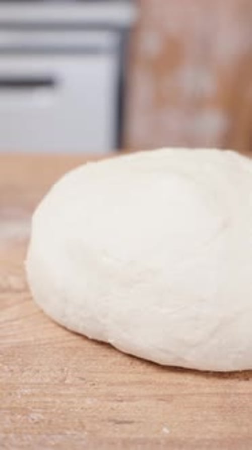 Vertical video. A lump of dough on a wooden table in the kitchen, slider.