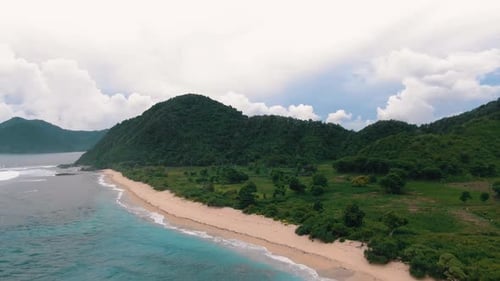 Aerial drone flying over an empty sandy beach. Wide ocean with islands and coastline on a cloudy day