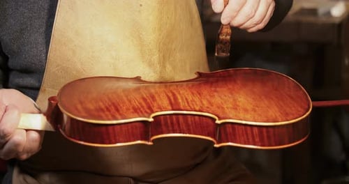 close up of luthier carefully applying varnish on a new hand crafted violin in his workshop