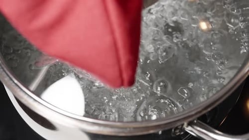 Boiling water in a silver pot, I, wearing a glove, slowly lift the glass lid in slow motion