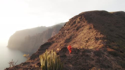 Person walking on a rocky mountain ridge at sunset overlooking the sea