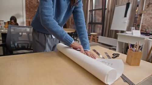 Biracial Male Architect Rolling out Paper Floor Plan on Table in Office