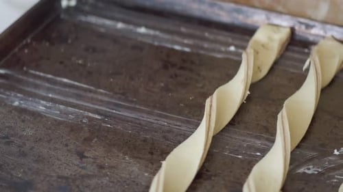 A baker places twisted dough pieces onto a baking sheet, preparing them for baking.