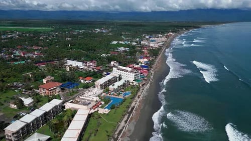 A wide drone shot captures a beautiful resort nestled along the shoreline, with the ocean's calm wav