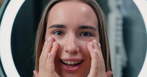 Close u of laughing girl applying moisturizing cream on her face. Portrait face of young beautiful