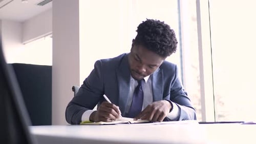 Young african american businessman writes ideas in notebook at his office desk