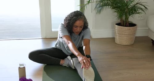 Starting seated on green mat, African American woman stretching hamstring for mobility