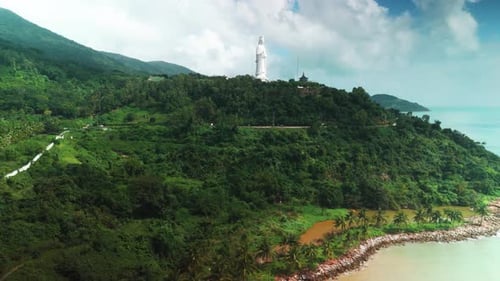 Giant white buddha statue standing tall on a forested mountain