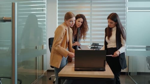 Three business women looking at laptop screen discussing subjects in the office.