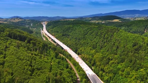 New highway through forest. Workers build a highway through lush hills under a clear sky