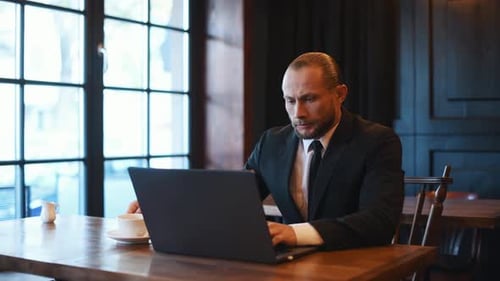Man in Suit Works on Laptop and Drinks Coffee