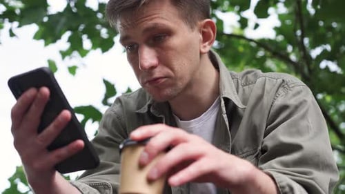 a Young Man Looking at His Phone the Park