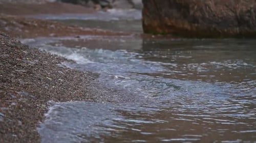 Gentle Waves Wash Over Pebble Beach Water Flows Around Rock in Tranquil Nature Scene Stream Trickle
