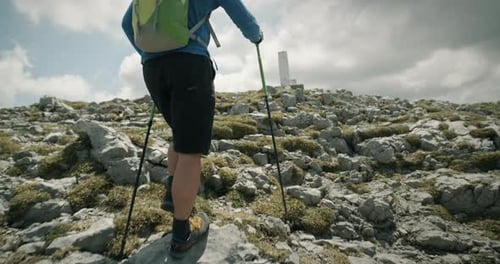 Camera tracking from behind a hiker with a green backpack walking with hiking poles towards the rock