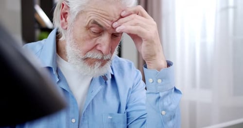 Close Up of Caucasian Old Greyhaired Man with Thoughtful Serious Face Working at Laptop Computer