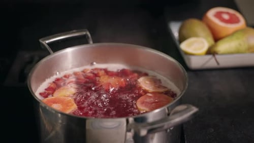 Une casserole de compote de fruits bouillante avec des tranches d'agrumes éclatantes, des poires fraîches, du citron et du pamplemousse