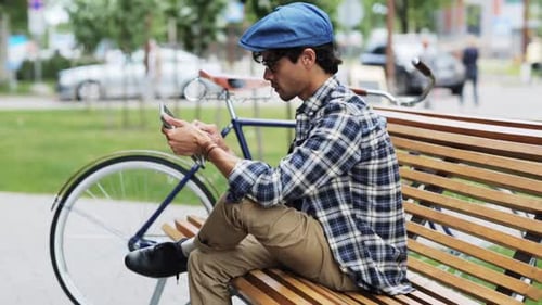 Creative hispanic man browsing tablet pc on city street bench next to fixie bicycle