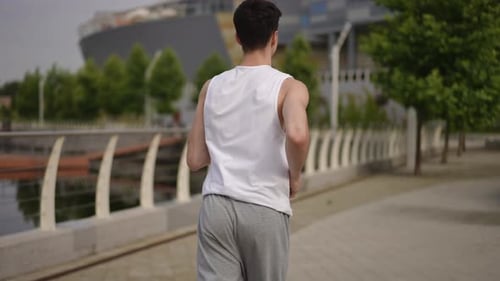Slow Motion Rear View A Young Male Athlete Jogging Outdoors on a Summer Morning in a City Park Along