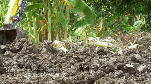 Digging and ploughing an empty field using a backhoe to prepare it for building and planting.