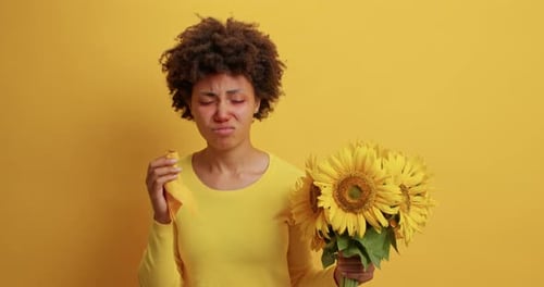 Woman with allergy symptoms holding sunflowers and tissue