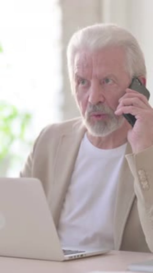 Senior Man Angrily Talking on Phone and Using Laptop