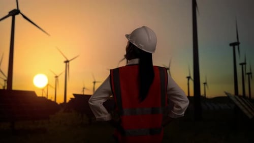 Akimbo, una ingeniera asiática con brazos, mira alrededor de las turbinas eólicas que giran