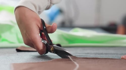 Close Up of Seamstress Cutting Fabric with Scissors Along Chalk Line