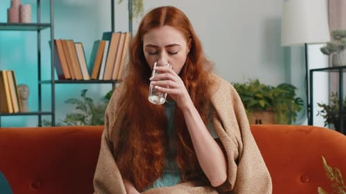 Woman with Headache Takes Pill on Couch