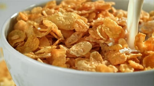 Milk Pouring onto Golden Cornflakes in White Bowl