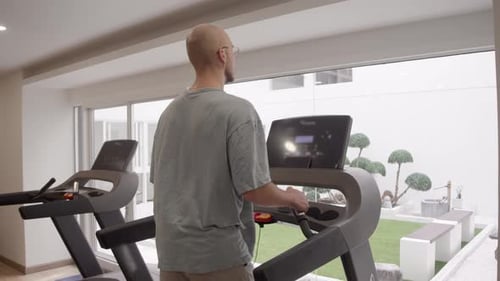 Back View Shot Captures Man Doing Treadmill Workout at Gym Hands Resting on Console While
