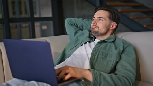 Relaxed Guy Lounging Couch Looking Laptop Screen at House Environment Closeup