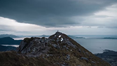 Small person standing with arms up in the air on top of a large mountain peak, watching over a beaut