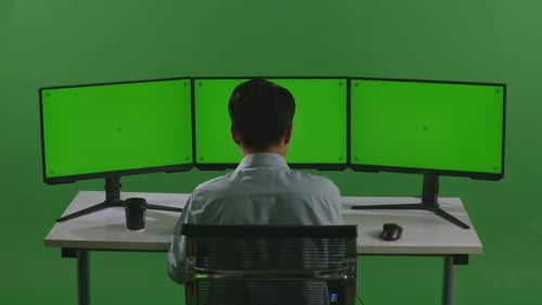 Vue arrière d'un homme asiatique travaillant avec une maquette de plusieurs écrans d'ordinateur dans un studio à écran vert