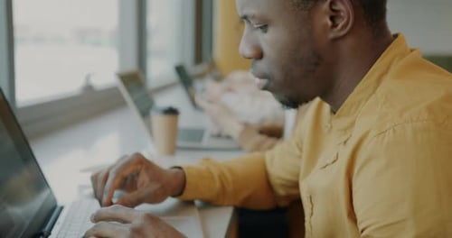 Gros plan d'un employé afro-américain utilisant la dactylographie sur ordinateur portable assis au bureau avec des collègues