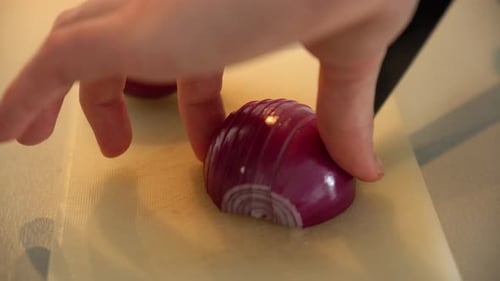 Hand dices purple onion with knife on cutting board