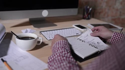 Man at desk looks through notebook, taking notes