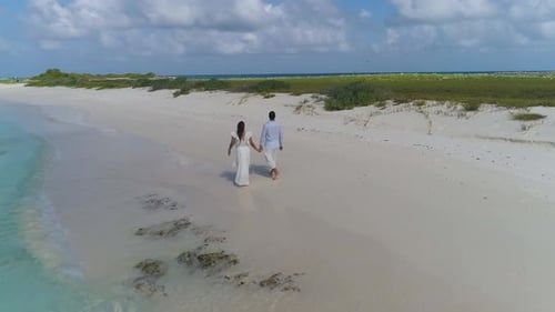 COUPLE WALKING ON sand beach hands to hands. Aerial view BLUE WATER CARIBBEAN SEA.
