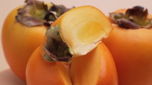 Several persimmons rotate while a juicy slice in front reveals the bright flesh.