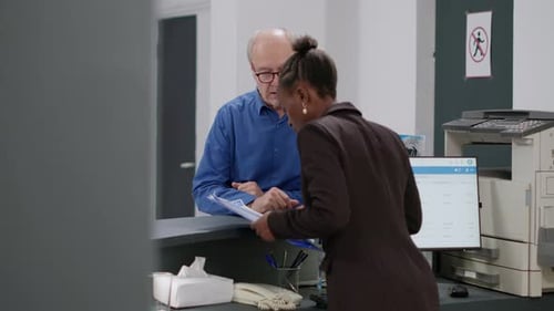 Man Signs Form at Medical Clinic Reception Desk