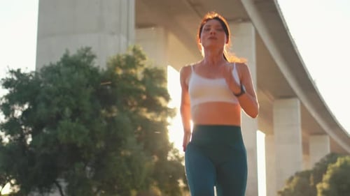 Sporty Woman Jogger Running Under Bridge During Sunny Day at City Park