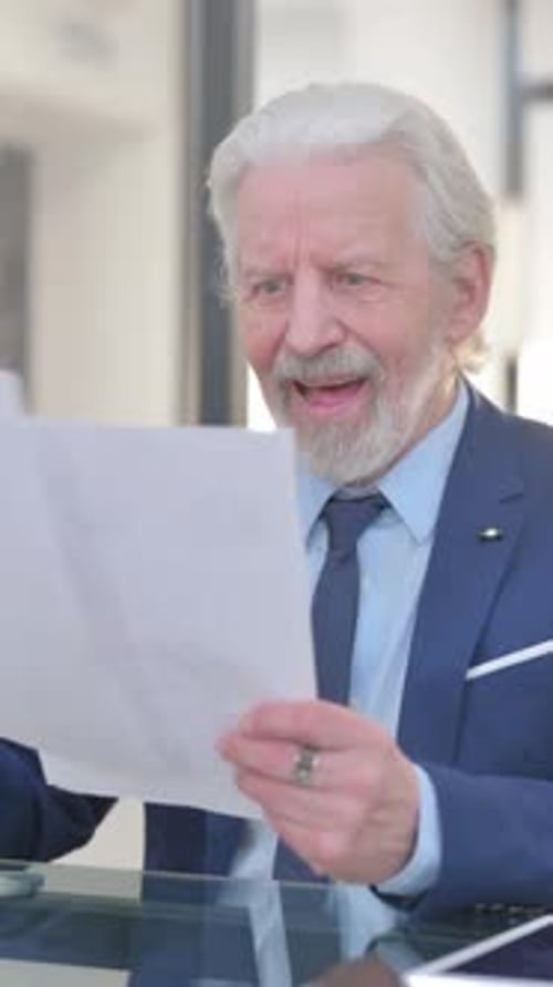 Smiling Senior Man Looks at Documents and Gives Thumbs-Up