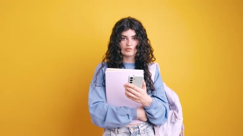 Student with Books and Phone on Yellow Backdrop