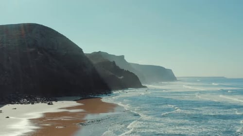 Breathtaking aerial view of Portugal coastline and cliffs. The sea is making waves for surfing.