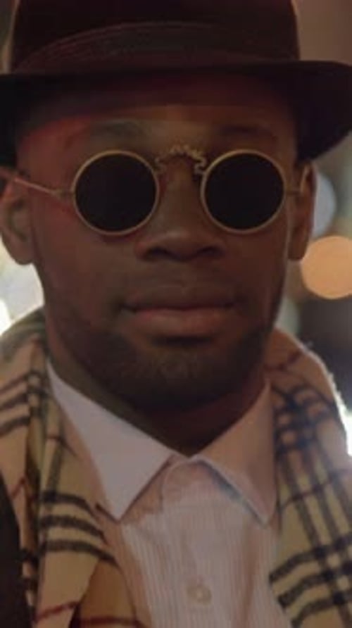 A Stylish Man Wearing Sunglasses and a Hat While Strolling Through the City at Night
