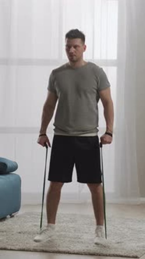 Focused Man Performing Resistance Band Workout at Home Standing on Soft Rug in Bright Living Room