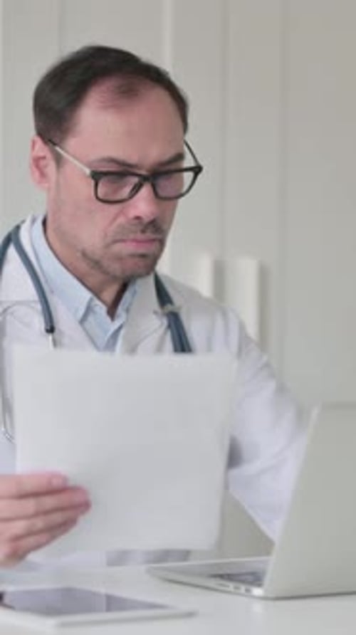 Médecin d'âge moyen avec ordinateur portable lisant des documents au bureau, Vidéo verticale