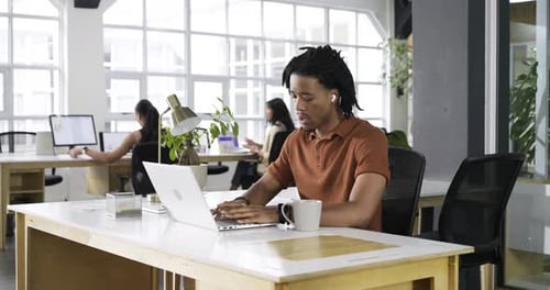 Commençant à travailler, un homme afro-américain tapant sur un ordinateur portable, se penchant en arrière puis tapant dans un bureau de coworking