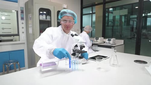 Scientist in lab coat using microscope and pipette